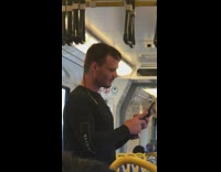 Guy with rat tail hair makes kissy face at phone on subway train