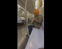 Person riding subway with pumpkin head using phone