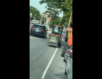Orange tractor with small dumpster dragging behind 