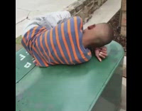 Little boy lays in fetal position on top of a trash bin outside, listening to Bruno Mars "Grenade" on his phone