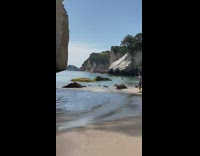 Woman pretends to hold boulder rock at beach and takes picture