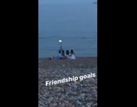 Four friends sit at beach and take picture with tripod set up