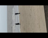 Woman long black coat spread hands feet beach