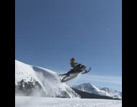 Brown jacket guy jumps black snowmobile mountain  