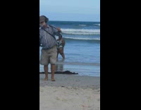 Girl dances beach shore guy metal detector 