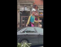 Person standing on sidewalk with giant puppet over their head
