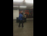Man in blue shirt dances to guy playing the saxophone in subway station