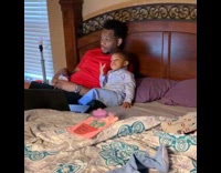 Dad and baby son eat snacks and watch TV together on the bed