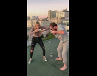 Guy and woman shotgun beer on green rooftop and spill on the floor, girl burps and spits out beer