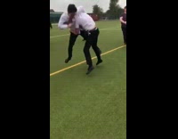 Two schoolboys in uniforms fight on soccer field in crowd of students