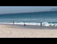 Woman in a black bikini kneels on the beach shore