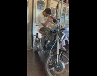 Guy brings motorcycle onto subway train and sits on it with head in his hands