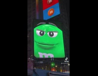 Man Stares at M-and-Ms Mascot Green in Big Screen