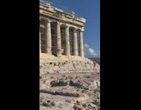 Woman in pink dress raises arms in front of the ruins