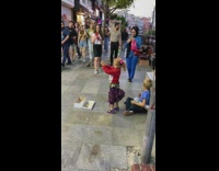 Little girl performer dancing on street while boy plays bongos