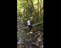 Guy sits on tree log branch rocks barefoot 