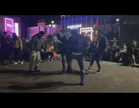 Three guys dance outside people sit watch 