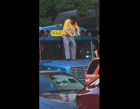 Guy stands on hood of blue school bus and plays air piano