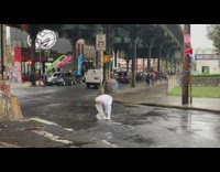 Guy in costume mask and white suit pushes ice down street 