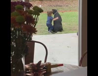 Little boy in blue shirt hugs black dog in backyard