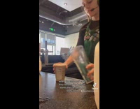 Woman in green starbucks apron pouring milk into drink and then mixing it with ice