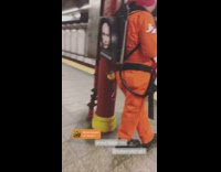 Man wears orange suit red beanie and Putin backpack in subway station