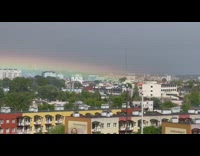 Less arch rainbow over trees and buildings