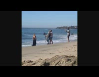 Woman black dress walk beach camera crew