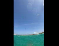 Guy in the water recording someone paragliding over his head 

