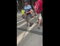 Person in Donald trump mask and business suit with chains on hands lays on sidewalk next to newspaper box