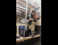 Man crouched on seat playing the violin on the subway