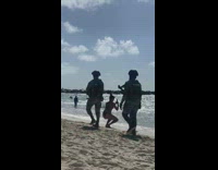 Two women in bikini poses while two marine walks behind them