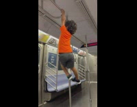 Boy in orange shirt climbs and hangs on the train handles