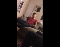 Guy sitting on couch in red shirt and dark blue pants wiggling legs