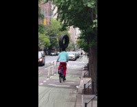 Man carry tire on head ride bike