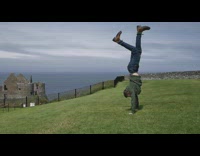 Guy tries to handstand on top of grass hill and  lands on neck