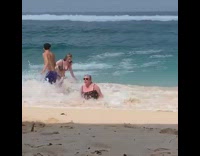 Woman gets swept off her feet and pushed by wave onto sand