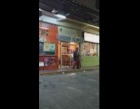 Shirtless guy wearing red pants dances outside restaurant 