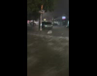 Car drives past cars parked in flood at night 