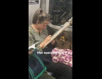 Woman cross stitching on subway train holds frame with a string tied to her ear