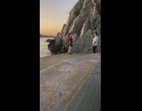 Woman black dress heels large rock beach