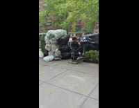 Woman uses elliptical bike work out machine on the sidewalk next to pile of trash