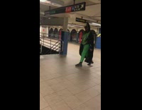 Man in green leaf outfit pants with cape walks in subway station