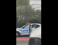 Police officer stands outside cop car and uses radar speed gun on oncoming cars on inside streets