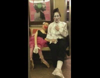 Girl dressed as a mime holds hands with a mannequin doll on subway train
