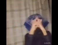Gang member with blue  and black bandana covering face does gang signs to a rap song