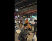 Guy in red yellow finger outfit sings and raps into speaker while riding rollerblades