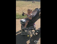 Baby in stroller at park holding speaker playing music while dancing