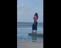 Woman in pink top and black skirt poses at the beach