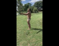 Black speedo guy stands barefoot grass beer